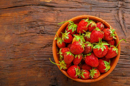 Ripe strawberries in a clay plate on a wooden table.の写真素材