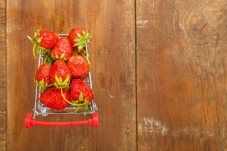 berries of a red strawberry in a grocery cart on a wooden background.の写真素材