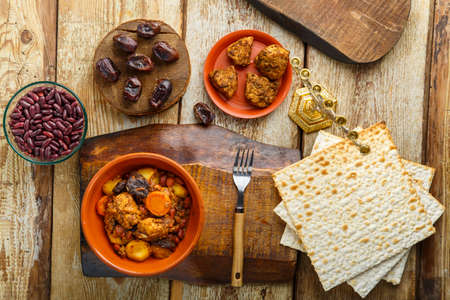 Jewish dish chelnt with meat on a stand next to matzo, fork and ingredients.の写真素材