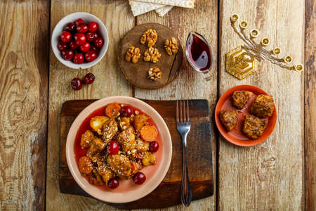 Jewish dish stewed potatoes with chicken in cherry sauce decorated with cherries on a stand next to the ingredients.の写真素材