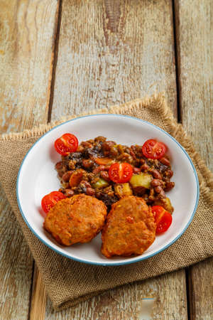 Cod cutlets with stewed potatoes and vegetables on a plate on a napkin on the table.の写真素材