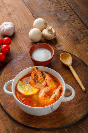 Tom yam soup with shrimps and coconut milk on the table on a round board next to coconut milk and tomatoes.の写真素材