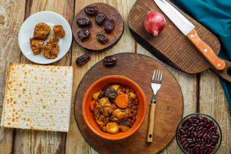 Jewish dish chelnt with meat on the table in a plate near ingredients and matzo. Horizontal photoの写真素材