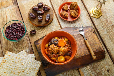 Jewish dish shuttle with meat in a clay dish on a wooden table near matzo and ingredients. Horizontal photoの写真素材
