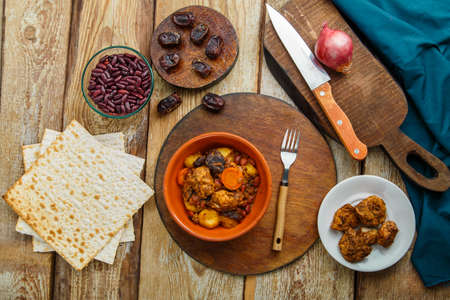 Jewish dish chelnt with meat in a plate on a wooden table on a stand next to a knife and ingredients. Horizontal photoの写真素材