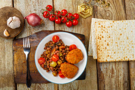 Cod cutlets with stewed potatoes and vegetables on a plate next to matzo and ingredients. Horizontal photoの写真素材