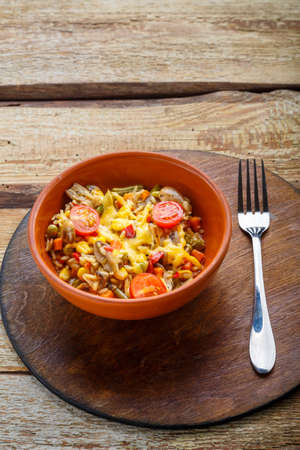 Risotto with mushrooms in a clay plate on a wooden background on a round board near a fork. Vertical photoの写真素材