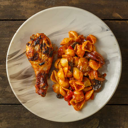 Seashell pasta in tomato with chicken leg baked on the grill on a wooden table. Square photoの写真素材