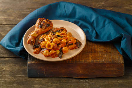 Seashell pasta in tomato and grilled chicken leg on a blue napkin. Horizontal photoの写真素材