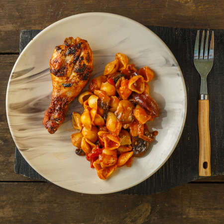 Seashell pasta in tomato with chicken leg baked on the grill on a woodenの写真素材