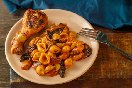 Seashell pasta in tomato and grilled chicken leg on a blue napkin next to a fork.の写真素材