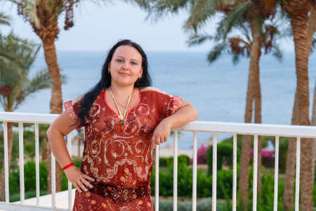 Happy brunette woman stands on the balcony against the background of the sea.の写真素材