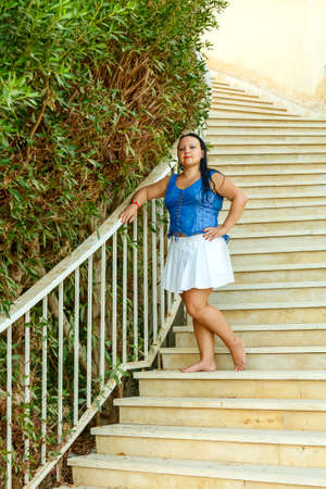 A brunette woman in a white skirt stands on a spiral staircase entwined with greenery.の写真素材