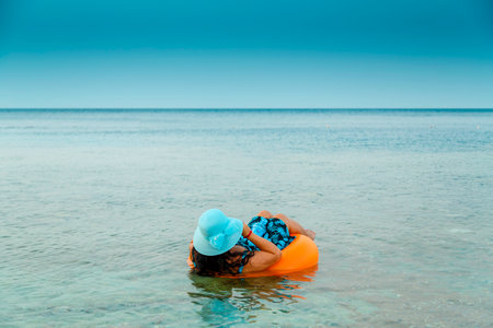 A woman in a straw hat and glasses in the sea in a swimming circle with a cocktail in her hand view...