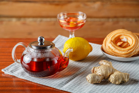 A kettle of strong hot tea on the table on a napkin next to lemon, ginger and jam and donuts. Horizontal photoの写真素材