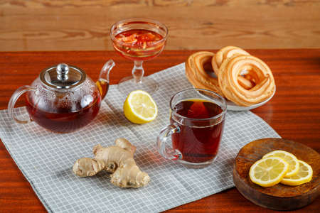 On the table is a teapot and a cup of strong tea, on a napkin with lemon and ginger, sweets in a vase. Horizontal photo Horizontal photoの写真素材