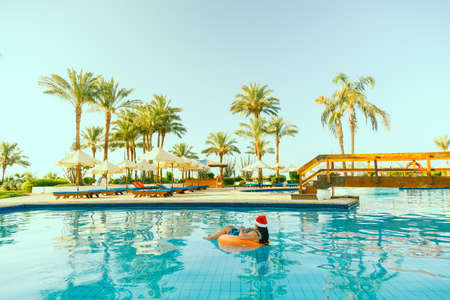 Young brunette woman in santa claus hat in a swimming circle in the pool during christmas holidays....