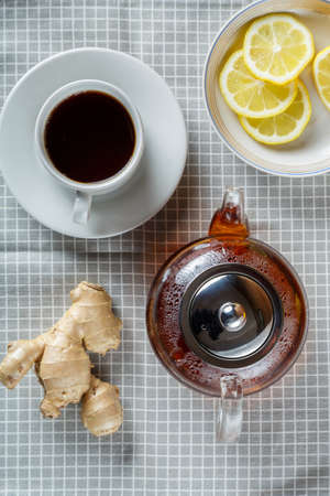 Teapot and a cup of strong aromatic tea on the table next to ginger and lemon top view. Vertical photoの写真素材