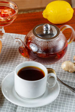 A teapot and a cup of strong aromatic tea on the table next to ginger and lemon ldem and donuts. Vertical photoの写真素材