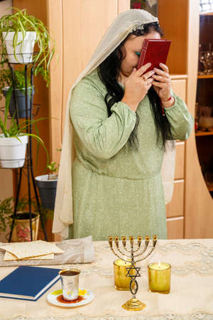 Jewish brunette woman in a cape on her head presses the siddur to her forehead.の写真素材