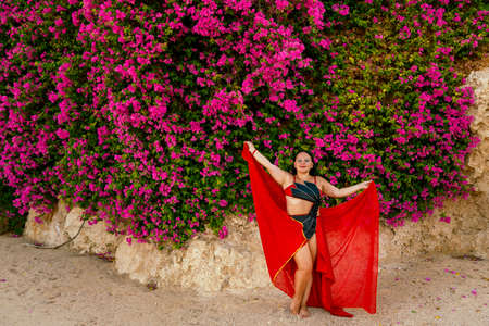 A woman in a red costume dances an oriental dance with a headscarf among flowering bougainvilleas.の写真素材