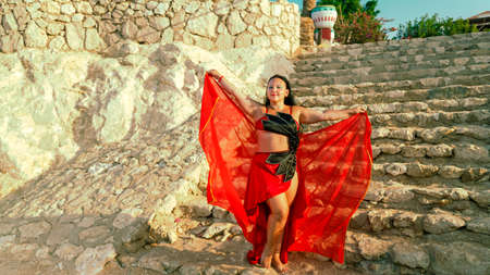 A woman in a red costume dances an oriental dance on a stone staircase. horizontal photoの写真素材