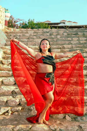 A brunette woman in a red oriental dance costume is dancing. vertical photoの写真素材