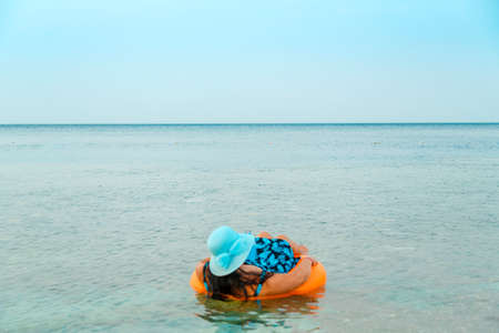 A woman in a straw hat and glasses in the sea in a swimming circle with a cocktail in her hand view...