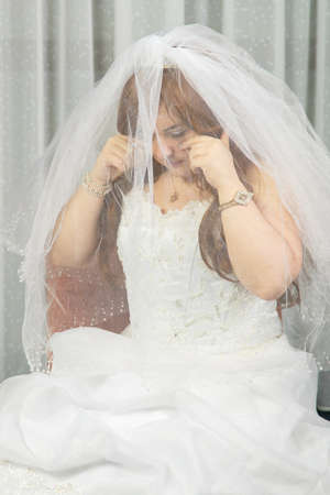 A Jewish bride in a room before the Hupa ceremony in a wedding dress with her face covered with a veil wipes tears from her eyes and is nervous. vertical photoの写真素材
