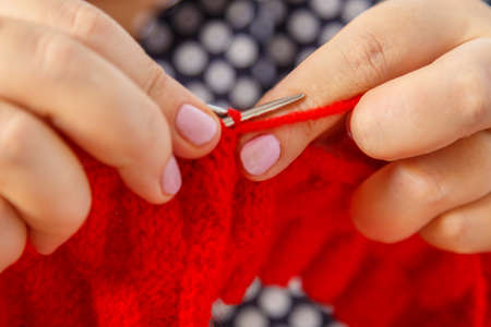 Knitting needles in female hands are knitted from red yarn close-up. horizontal photo