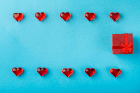 On a blue background, a box with a gift decorated with hearts with red pebbles save a place. horizontal photoの写真素材