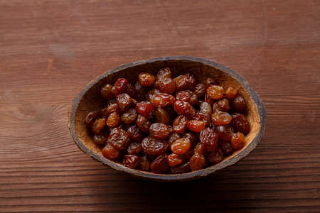 Raisins in a bowl of coconut shell on a wooden table. horizontal photo