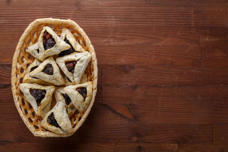 Gomentash with poppy seeds and prunes freshly baked for the Purim holiday on a wooden table in a wicker bread basket.copy space. horizontal photoの写真素材