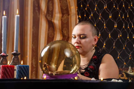 A bald woman fortuneteller reads the future on runes by candlelight in a magic salon. horizontal...