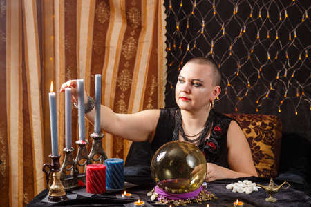 A bald woman fortuneteller lights candles in a magic salon. horizontal photoの写真素材