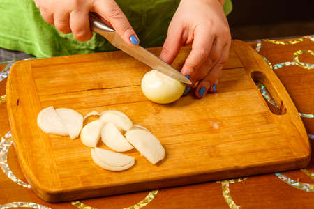 Women's hands cut onions with a knife on a wooden board. horizontal photo