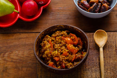 A plate of bulgur with vegetables and mushrooms on the table next to a wooden spoon and a cutting board. horizontal photoの写真素材