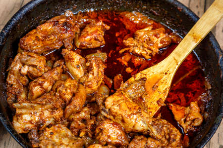 Fried chicken in spices and sauce is hot in a frying pan with a wooden spatula. horizontal photo