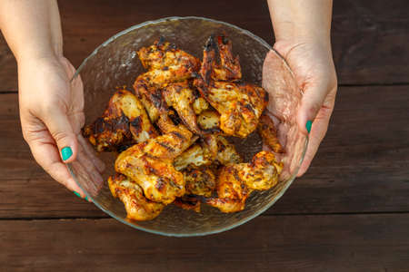 Female hands put a blue plate with grilled wings on a wooden table. horizontal photo