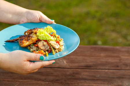 Female hands put on the table on the street table a plate with chicken and vegetables next to a dish...