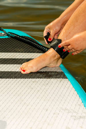 A woman's hands fasten a SUP board safety line to her leg before sailing. vertical photoの写真素材