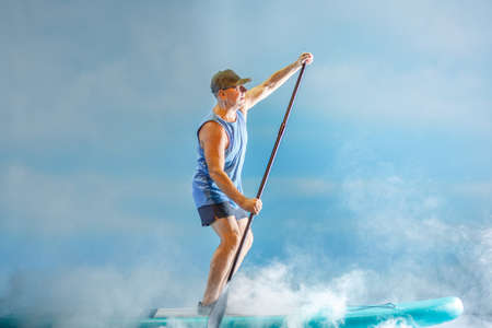A man on a sub-board with an oar paddles in thick fog against the background of clouds. horizontal...