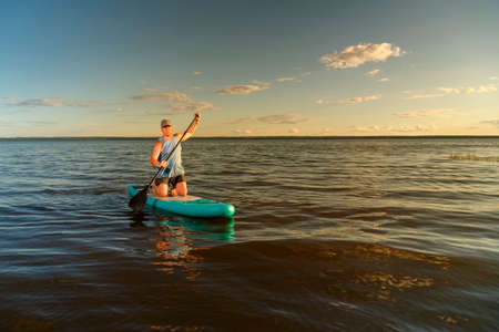 a man in shorts stands with a paddle on a SUP board at sunset in the lake. horizontal photoの写真素材