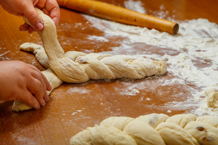 The hands of a Jewish woman weave a challah in the form of a pigtail for Shabbat on a wooden table. horizontal photoの写真素材
