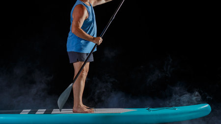 A man without a face on a sub board with a paddle on a black background in the fog. horizontal photoの写真素材