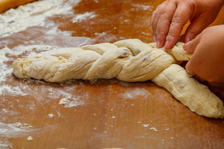 The hands of a Jewish woman weave a challah in the form of a pigtail for Shabbat on a wooden table. horizontal photoの写真素材