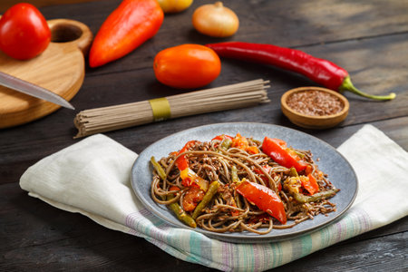 Soba with vegetables in soy sauce sprinkled with flax seeds in a plate on a napkin next to onions,...