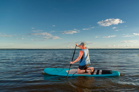 A man on his knees on a sup board in the evening at sunset. horizontal photoの写真素材