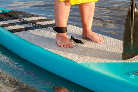 Women's legs standing on a sapboard with a paddle floats on the water. horizontal photoの写真素材