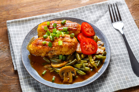 Green beans with champignons and cutlets sprinkled with green onions in a plate on a wooden table on a gray napkin next to a fork. horizontal photoの写真素材